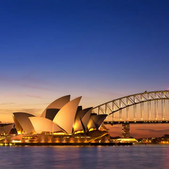 Australien – Blick auf das Opernhaus von Sydney in der Dämmerung mit farbenprächtigem Himmel und beleuchteter Brücke.