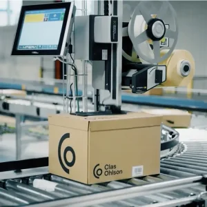 Ein Karton wird an einer Produktionslinie oben mit dem automatischen Etikettierer der MPERIA A-Serie etikettiert.