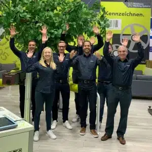 Ein fröhliches Team mit erhobenen Händen auf einer erfolgreichen Messe