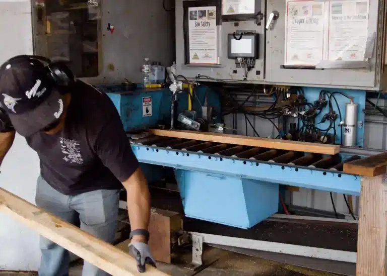 Arbeiter, der neben industriellen Produktionsanlagen mit Schnittholz hantiert