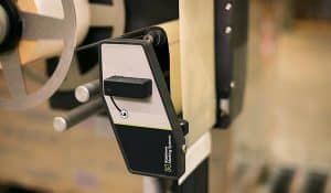 Nahaufnahme eines automatischen Palettenetikettierers der A-Serie von „ Matthews Marking Systems “, der bei „ akkurate Platzierung der Etiketten “ in der industriellen Verpackungsproduktion zum Einsatz kommt.