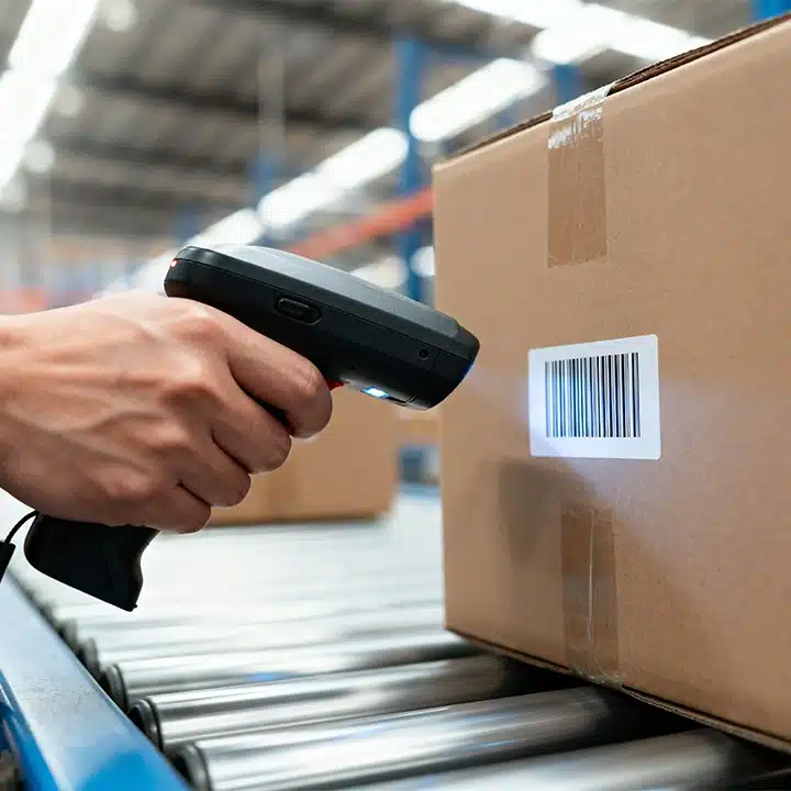 Ein Lagerarbeiter scannt mit einem Hand-Barcodescanner ein Versandetikett auf einem Karton, der auf einem Förderband vorbeiläuft.