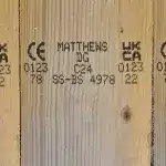 Holzbrett mit aufgedruckten UKCA- und CE-Konformitätszeichen, Matthews-Identifikationscodes und weiteren Produktinformationen.